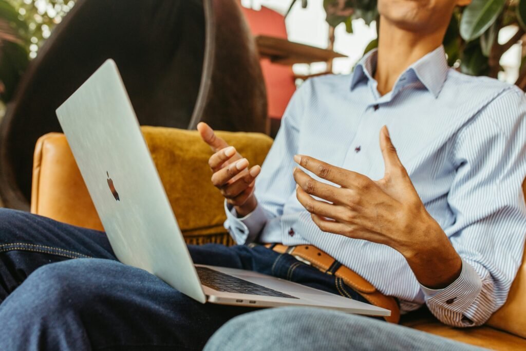 Close-up of a man gesturing while browsing on a laptop indoors, relaxed setting.